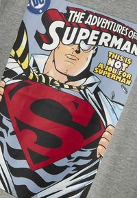 Grijze t-shirt met een grote, kleurrijke Superman comic print, met een gedurfde rode "S," zwart-witte details, en een gele gestreepte das.