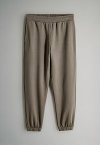 Pantaloni sportivi color taupe con elastico in vita e alle caviglie, dotati di tasche laterali, esposti su uno sfondo chiaro e semplice.