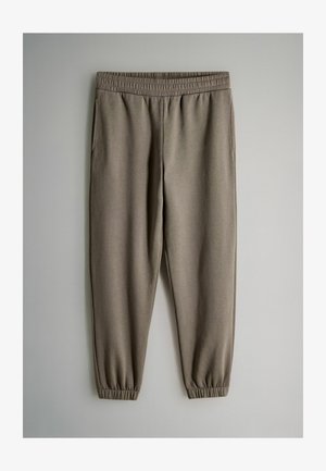 Pantalons de survêtement couleur taupe avec taille élastique et poignets, dotés de poches latérales, présentés sur un fond clair.