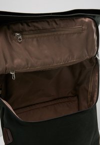 Wnętrze czarnego plecaka materiałowego z brązowym wykończeniem, z zamknięciem na zamek błyskawiczny u góry oraz dodatkową kieszenią na zamek po jednej stronie dla lepszej organizacji.