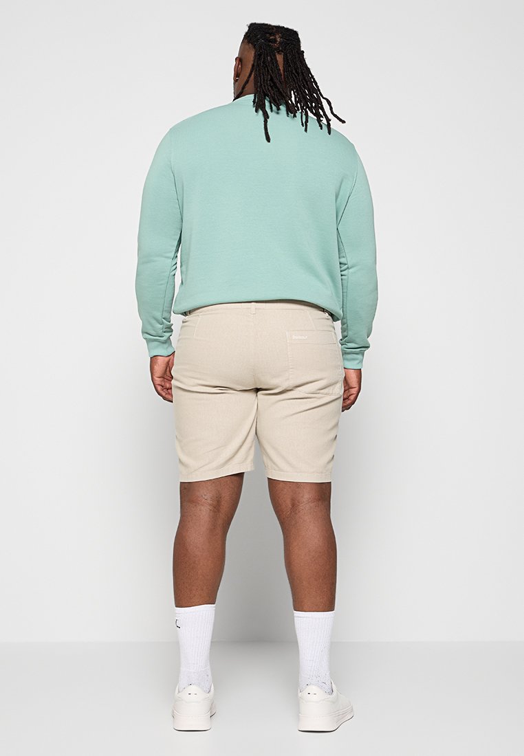 Miętowozielona bluza i beżowe szorty w połączeniu, z luźnym krojem i minimalistycznym designem. Białe trampki i skarpetki do kostek.