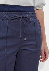 Dunkelblaue Joggings mit Kordelzug, ausgestattet mit einer glatten Textur, elastischem Bund und silbernen Hardware-Details an den Kordeln.
