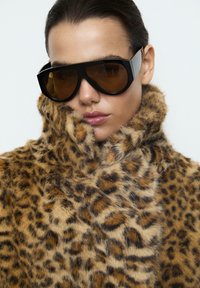 Leopardenmuster Kunstfellmantel mit hohem Kragen, weicher Textur; übergroße schwarze Sonnenbrille mit bernsteinfarbenen Gläsern, minimalistischem Design.