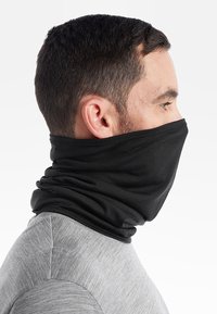 Svart halsduk gjord av mjukt, stretchigt tyg. Har en slät textur och sömlös design, bärs över en grå skjorta.