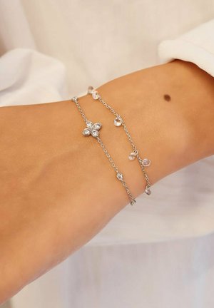 Ankel prydet med to fine sølvkædeankler, en med små krystalkugler og en blomstformet krystalklynge.