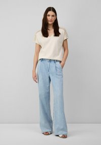 Haut crème à manches courtes avec des accents texturés, associé à un jean large bleu clair, avec une taille haute et un design classique à 5 poches.