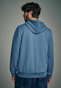 Felpa con cappuccio in tessuto azzurro chiaro testurizzato, caratterizzata da un orlo e polsini a coste, cucitura del cappuccio visibile e una vestibilità comoda.