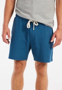 Blå teksturerede shorts med elastisk talje, featuring en beige snorlukning og sidelommer. Bæres med en grå skjorte.