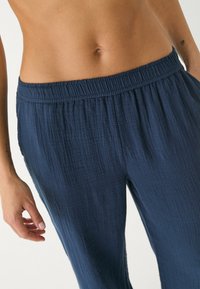 Pantalon en tissu léger bleu marine froissé, avec une taille élastique et des poches latérales, offrant une coupe décontractée.