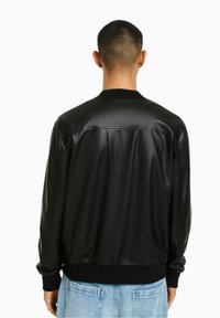 Giubbotto bomber in pelle nera con colletto e polsini a costine. Texture liscia, design aderente e dettagli sulla vita. Visto da dietro.