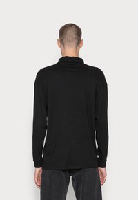 Czarna koszula z długim rękawem z klasycznym kołnierzykiem, o miękkiej fakturze i luźnym kroju. Widok z tyłu pokazuje prosty, minimalistyczny design bez wzorów.