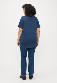 Σκούρο μπλε μπλουζάκι κοντομάνικο με χαλαρή εφαρμογή που συνδυάζεται με τζιν παντελόνι ίσιας γραμμής. Ο ύφασμα φαίνεται λείο, με γυρισμένα μανίκια.