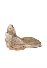 Espadrilky na klínu ve světle zlaté látce s texturovanou juteovou patou. Mají špičku, omotání kolem kotníku a detaily z přírodních vláken.