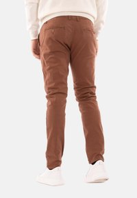 Pantaloni in cotone marrone a taglio slim, con due tasche posteriori e frontale piatto. Abbinati a sneakers bianche.