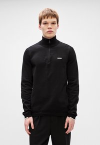 Pullover preto de malha com gola com zíper, apresentando uma textura canelada e um pequeno logótipo branco "BOSS" no lado esquerdo do peito. Design simples e ajustado.