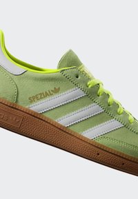 Gröna mockaskor med tre vita ränder, gula detaljer och en brun gummisula. Har "SPEZIAL"-logotyp nära snörningsområdet.