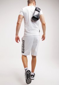 Shorts deportivos grises con el logo de "adidas" en negro. Camiseta blanca. Guantes de boxeo negros colgados del hombro. Zapatillas deportivas en blanco y negro.