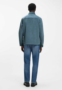 Dunkelblaue Cordjacke mit geknöpften Manschetten, geradem Schnitt und legerer Passform, kombiniert mit hellblauen Jeans und schwarzen Schuhen.