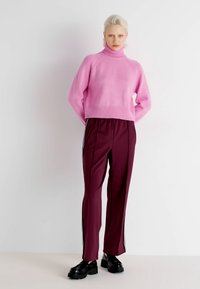 Pink knitted turtleneck sweater paired with maroon track pants featuring side stripes and black platform shoes. Smooth texture, relaxed fit.