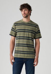Oliven grøn T-shirt med striber i marineblå og lyseblå, korte ærmer, rund hals og et lille logo på venstre bryst.