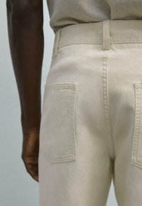Beige cotton pants featuring a straight fit, visible back pockets, and a smooth texture with subtle stitching details along the seams.