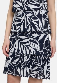 Granatowa sukienka z białymi wzorami liści, w warstwach falban, krótka długość i miękka tekstura materiału.