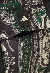 Black fabric bag featuring a green and white paisley pattern, zippered pocket, and a small white logo tag. Textured material finish.
