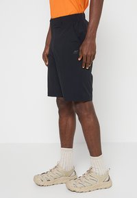 Czarne szorty wykonane z lekkiego, elastycznego materiału, z elastyczną talią i bocznymi kieszeniami. W zestawieniu z jasnym, otwartym obuwiem.