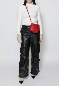 Pantaloni cargo in pelle nera con tasche con cerniera, abbinati a un top bianco con collo alto e a una piccola borsa a tracolla in pelle rossa. Scarpe nere a punta.