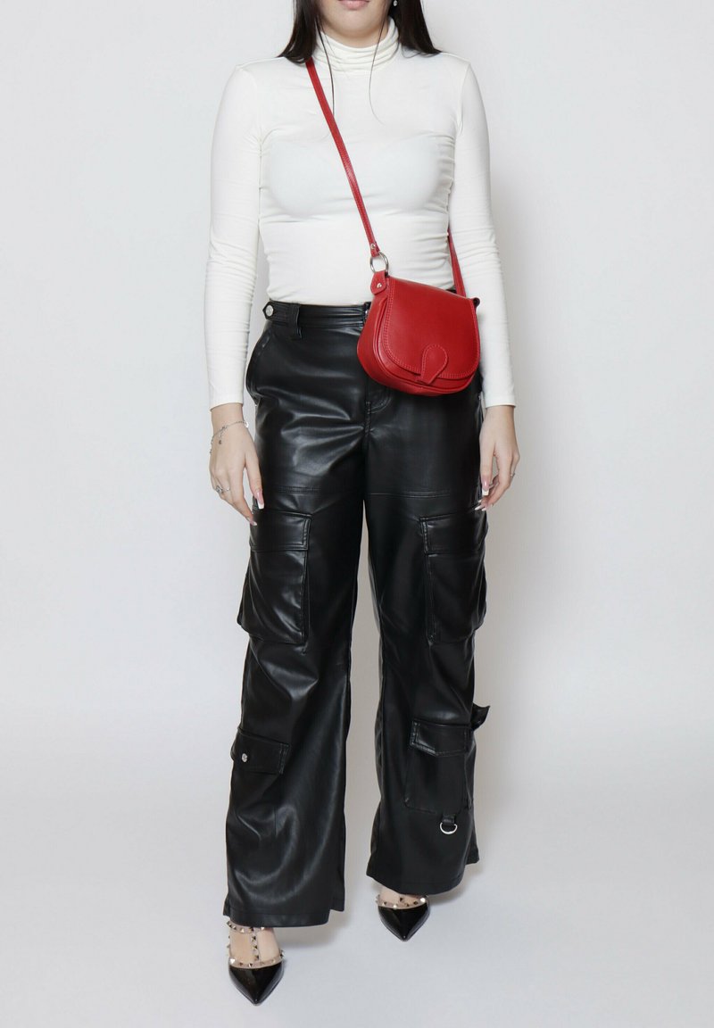 Pantaloni cargo in pelle nera con tasche con cerniera, abbinati a un top bianco con collo alto e a una piccola borsa a tracolla in pelle rossa. Scarpe nere a punta.