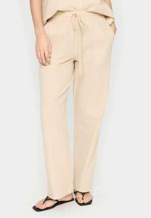 Pantaloni lounge beige leggeri con vita elastica e cordino regolabile. Presentano due tasche laterali e un tessuto testurizzato.