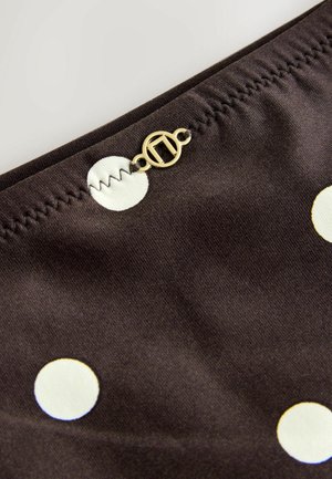 Pruun kangas valgete täpikestega, millel on volditud õmblus ja kuldne ümmargune sulgemisdetail. Suumvaade tekstiuri struktuurile.