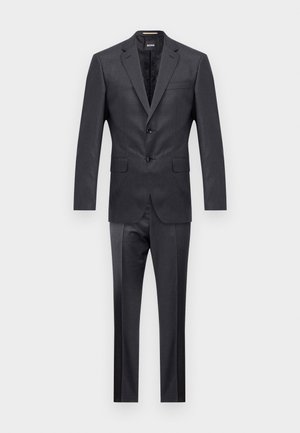 Traje gris oscuro con chaqueta de un solo botón, solapas de muesca y pantalones de frente plano. Tejido texturizado con un sutil brillo y un ajuste a medida.