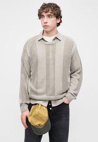 Ανοιχτό γκρι πλεκτό πουλόβερ με υφασμένο ριγέ μοτίβο, σε φαρδιά εφαρμογή, φορεμένο πάνω από πουκάμισο με γιακά, συνδυασμένο με σκούρα τζιν και καπέλο μπέιζμπολ.