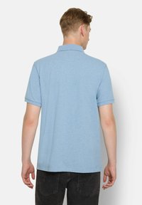 Hellblaues Polohemd mit kurzen Ärmeln und klassischem Kragen, aus einem weichen Stoff gefertigt. Sichtbare Nähte entlang dem Saum und dem Kragen.