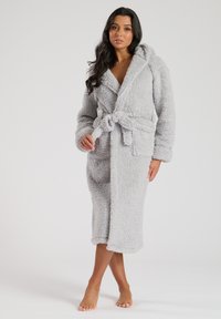Peignoir de bain gris clair, moelleux, avec capuche, manches longues, ceinture et poches. Longueur mi-mollet avec un tissu texturé et doux.