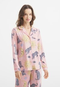 Conjunto de pijama rosa que presenta estampados de sol y leopardo, blusa con botones y cuello, mangas largas, y pantalones a juego con patrones similares.