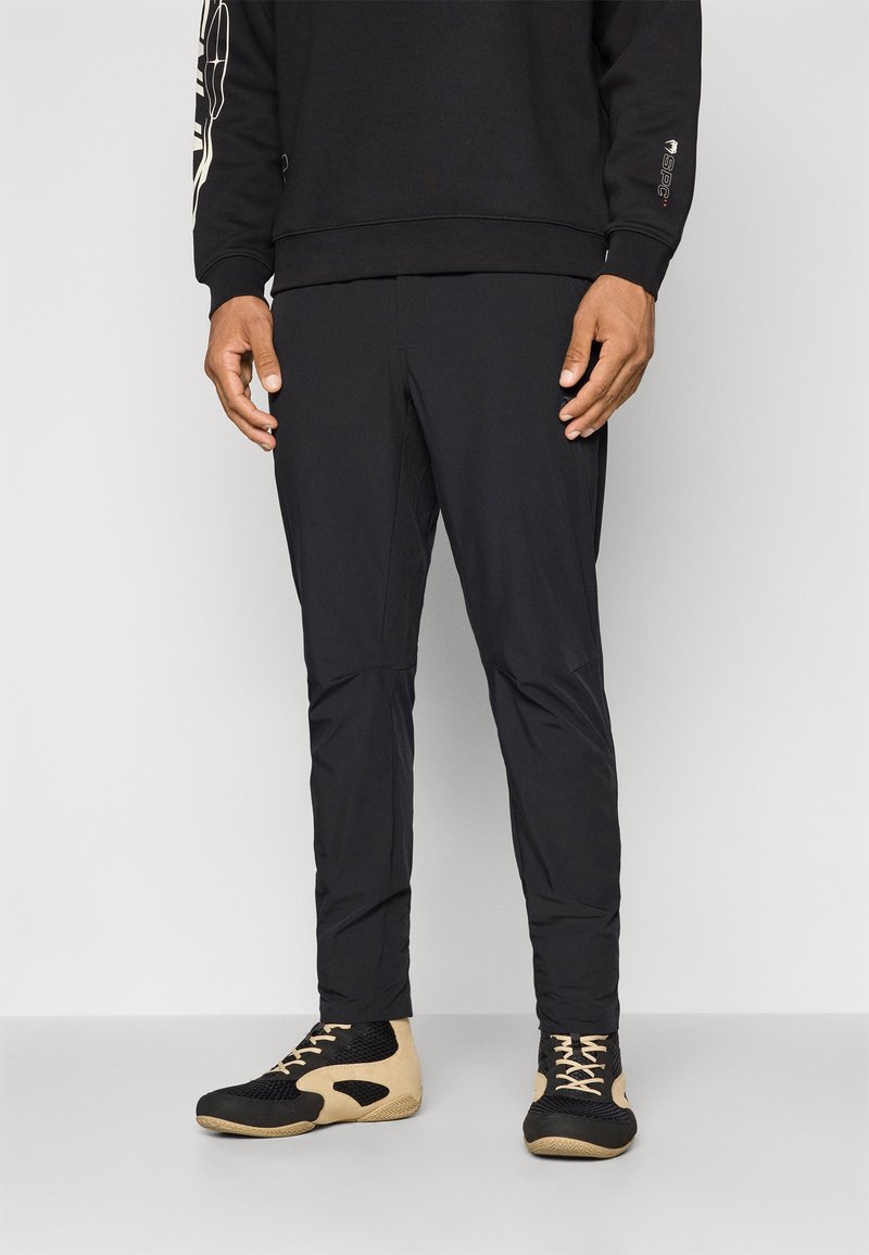 Black athletic pants with tapered legs, made from a lightweight, textured fabric. Paired with black and beige high-top shoes.