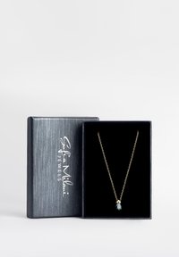 Guldkæde med en dråbeformet lyseblå gemstone vedhæng, præsenteret i en sort udslagskasse med en struktureret grå ydre.