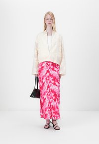 Hvit brodert bomberjakke, rosa tie-dye maxiskjørt, svarte sandaler med stropper og en liten svart veske. Glatte teksturer og lett stoff.