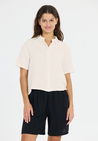 Korte mouwen, lichtgewicht roomkleurige blouse met een kraag, gecombineerd met zwart gestructureerde shorts. Heeft een iets verkort ontwerp en een relaxte pasvorm.