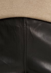 Un tissu en tricot beige se superpose à un cuir noir lisse, présentant une couture visible. Le cuir a une texture grainée subtile et un éclat doux.