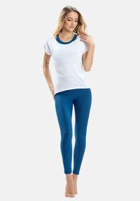 Fehér, rövid ujjú póló, amelyet teal színű, testhezálló leggings-szel párosítottak. A pólón kerek nyakkivágás található, a leggings sima és rugalmas.
