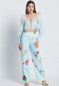 Blue crop jacket with transparent ruffled collar, paired with matching wide-leg pants featuring colorful patterns and illustrations. Gold hardware accents.