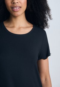 Svart randig t-shirt med rund halsringning och korta ärmar som har en volangkant. Tyget verkar mjukt och texturerat.