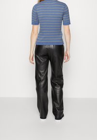 Blå och grön randig stickad topp med korta ärmar, i kombination med hög midja svarta läderbyxor som visar en slät och glänsande textur.