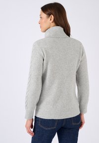 Suéter de canalé gris claro con un cuello alto y detalles de punto trenzado en las mangas. Tiene un corte relajado y está hecho de un material suave y texturizado.