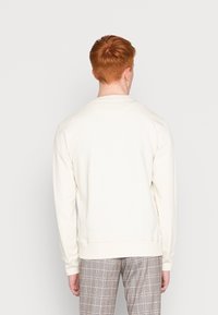Sudadera de color crema con mangas largas, puños acanalados y un cuello redondo, combinada con pantalones de cuadros.