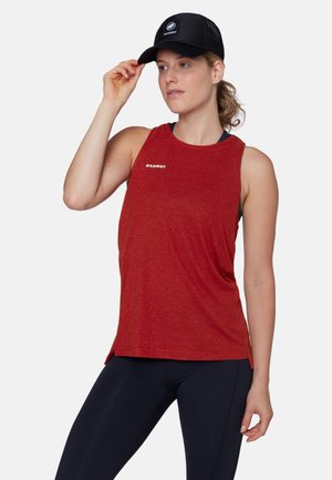 Donna che si sistema un berretto nero Mammut, indossa una canotta rossa Mammut senza maniche e leggings neri, rivolta leggermente verso destra su uno sfondo neutro.