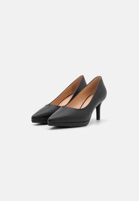 Črne usnjene visoke petke s koničasto obliko in ozkim stiletto petom. Notranjost ima gladek bež podlog.